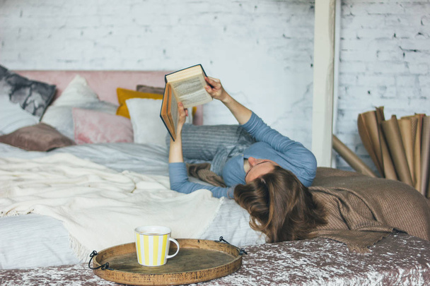 Young woman reading book on bed in loft room, slow life - Photo, image