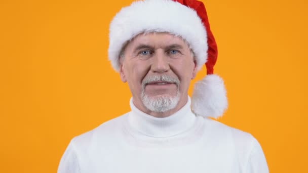 Mature man in santa hat showing quiet gesture, holiday surprise, secret party - Πλάνα, βίντεο