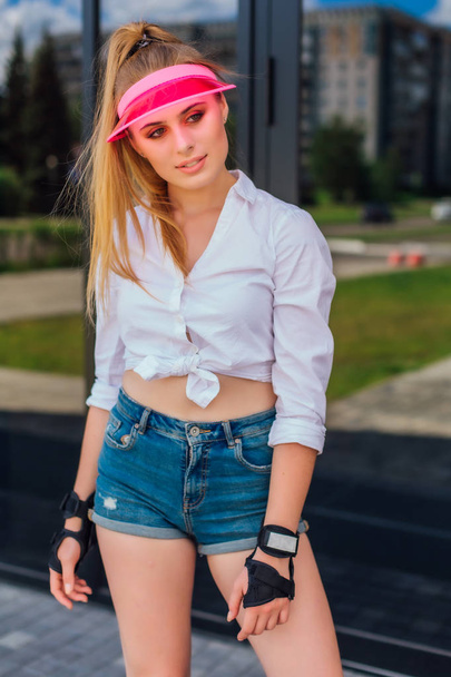 Portrait of an emotional girl in a pink cap visor and protective gloves for rollerblades and skateboarding. - Foto, Bild