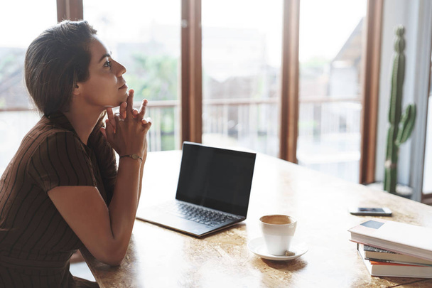 Attractive lucky successful businesswoman listening employees reports sit satisfied pleased near window, laptop opened drink coffee hold hands above chin thoughtful, thinking make decision - Foto, Imagen
