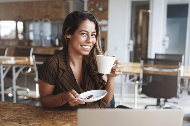Joyful attractive tanned hispanic woman sit cafe giggling having fun enjoy pleasant carefree conversation look camera adorable smile hold small plate drink coffee, relaxing with friend - Foto, afbeelding