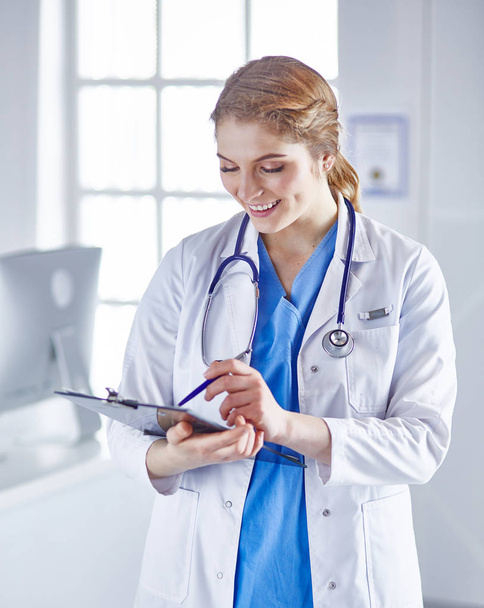 Young woman doctor is standing with board with clipboard smilin - Photo, image