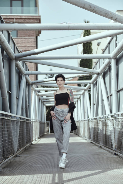 Raven haired young lady with tattoos posing on the bridge - Photo, Image