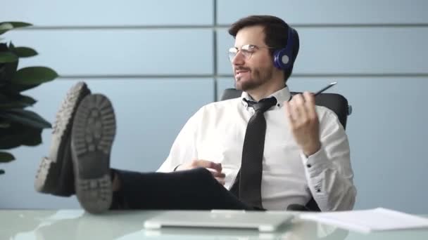 Happy businessman wearing headphones listening to music at workplace - 映像、動画