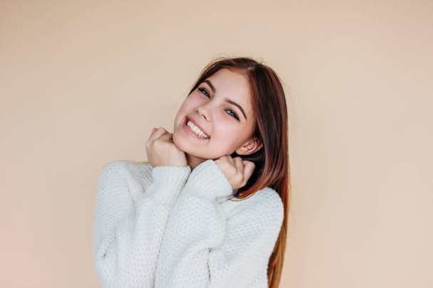 Beautiful smiling girl with clean skin and dark long hair in cozy white sweater on beige background - Foto, immagini