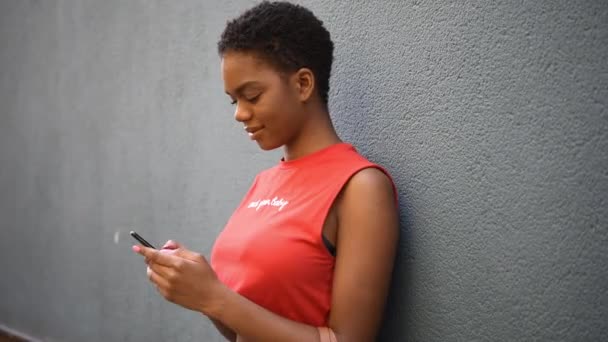Νέα μαύρη γυναίκα μηνύματα με το έξυπνο τηλέφωνό της σε αστικό φόντο. - Πλάνα, βίντεο