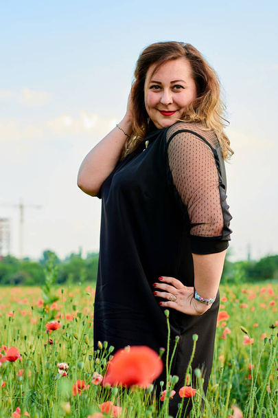 Donna più grande in un abito nero su un campo di grano verde e papaveri selvatici. sovrappeso grasso donna
. - Foto, immagini