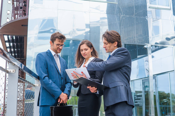 Confident businesspersons talking in front of modern office building. Businessmen and businesswoman have business conversation. Banking, professional job and financial market concept. - Foto, Imagem