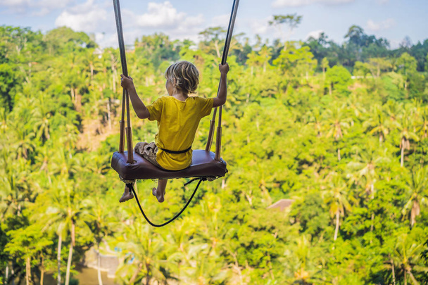 Young boy swinging in the jungle rainforest of Bali island, Indonesia. Swing in the tropics. Swings - trend of Bali. Traveling with kids concept. What to do with children. Child friendly place - Foto, Imagen