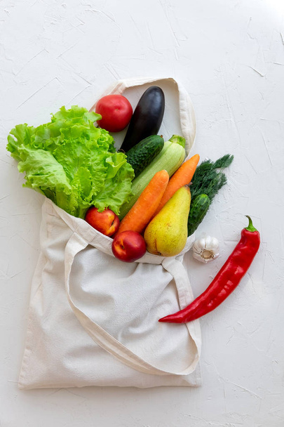 Textile bag filled with vegetables and fruits, top view on white - Foto, Bild