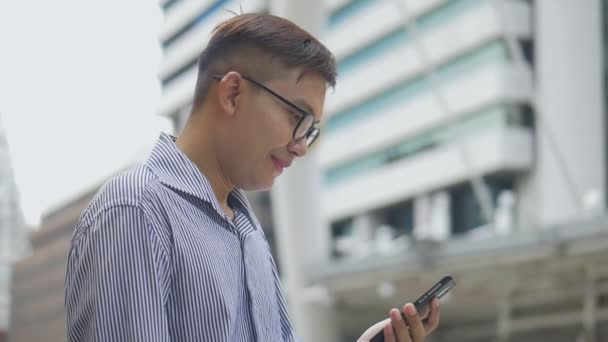 Slow-motion portrait Asian businessman answers the phone. An Asian man with glasses uses a phone in the street near a big office building. - Filmmaterial, Video