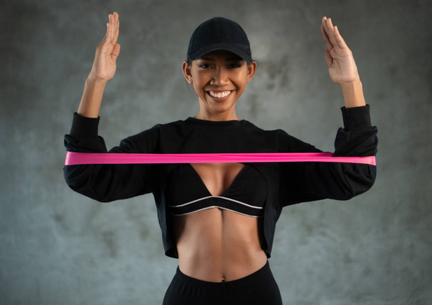 Happy healthy smiling woman working out with resistance band at the gym. Sportswoman performs exercises for the muscles of the chest - Photo, Image