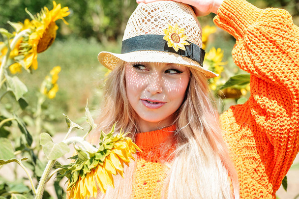 Mooie blanke vrouw in oranje Sweatshirt poseren op weide met zonnebloemen. - Foto, afbeelding