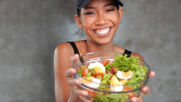 Portré szép fiatal mosolygós nő, fekete póló gazdaság tálba egészséges salátát konkrét háttér - Fotó, kép