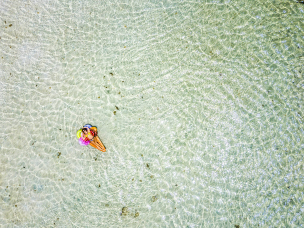 вид с воздуха на красивую молодую женщину, принимающую солнечную ванну, расслабляющуюся на надувном матраце лило в голубой тропической океанской лагуне
  - Фото, изображение