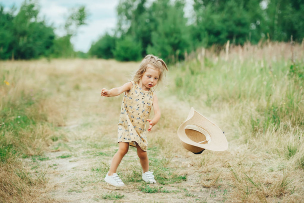 Doğada elinde şapka ile yeşil çim üzerinde eğlenen neşeli küçük kız.  - Fotoğraf, Görsel