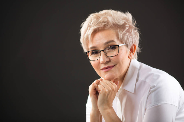 beautiful elderly woman in a white shirt and glasses on a black background - Фото, зображення