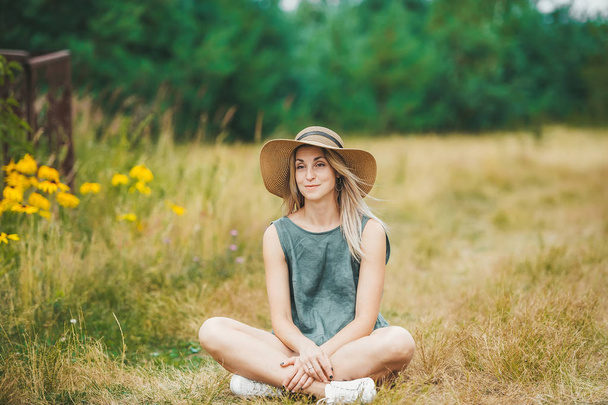 Smiling young woman in hat sit in lotus pose at summer meadow. - Photo, Image