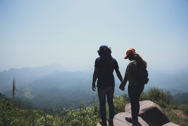 恋人カップルの女性と男性アジア人の旅行は休日にリラックスします。座って、山の風景を見てください。楽しそうにマウンテンパーク。山でハイキング。タイで - 写真・画像