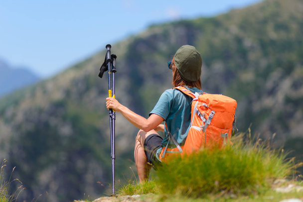 Woman hiker on mountain top with backpack and trekking poles, selective focus rear view, alps in background, summer fitness wellbeing - Foto, immagini