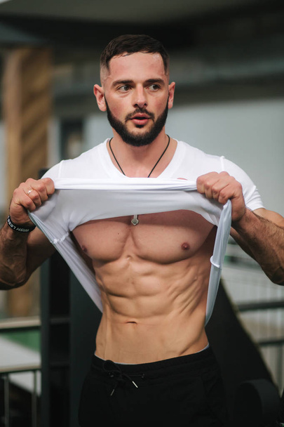 Young athlete posing with a torso for photography in gym. Bodybuilder, athlete with pumped muscles, breast and arm rescue. Man show abdominal muscles - Zdjęcie, obraz