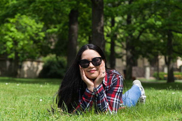 Young beauty woman in sunglasses  lying on grass. Sunny day in park. - Fotó, kép