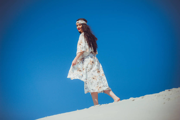 A young beautiful woman in beachwear and a ribbon on her head. Walking on the desert sand. - Photo, Image