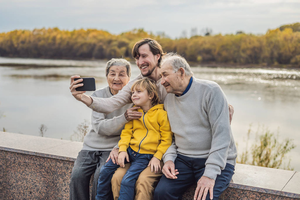 Pareja mayor con nieto y bisnieto tomar una selfie en el parque de otoño. Bisabuela, bisabuelo y bisnieto
 - Foto, imagen