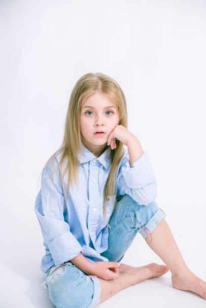 Beautiful fashionable little girl with blond hair in jeans clothes on a white background in studio - Фото, зображення
