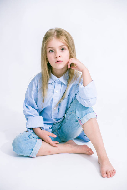 Beautiful fashionable little girl with blond hair in jeans clothes on a white background in studio - Fotografie, Obrázek