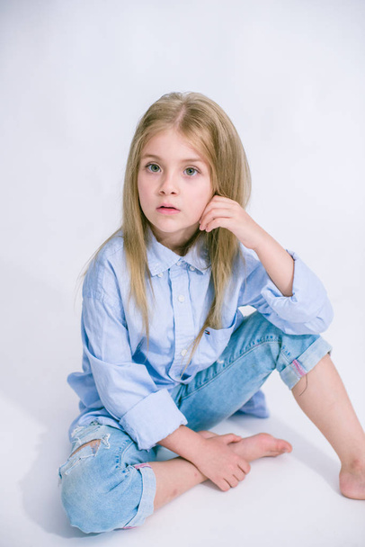 Beautiful fashionable little girl with blond hair in jeans clothes on a white background in studio - Foto, immagini