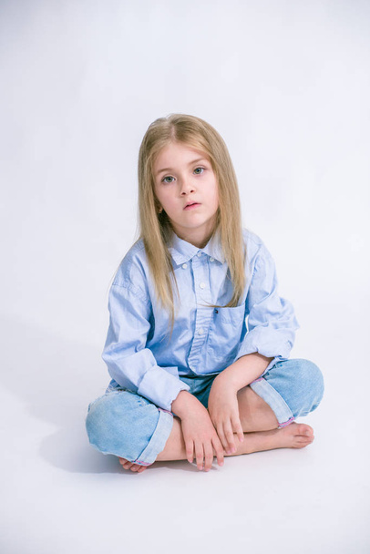 Beautiful fashionable little girl with blond hair in jeans clothes on a white background in studio - Valokuva, kuva