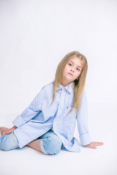 Beautiful fashionable little girl with blond hair in jeans clothes on a white background in studio - Foto, imagen