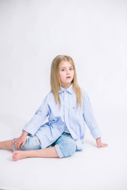 Beautiful fashionable little girl with blond hair in jeans clothes on a white background in studio - Foto, afbeelding