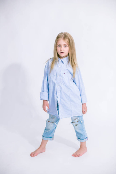 Beautiful fashionable little girl with blond hair in jeans clothes on a white background in studio - Фото, зображення