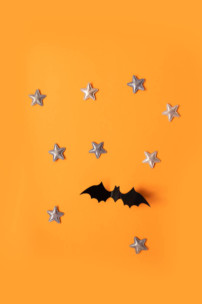 Halloween-Urlaubskonzept schwarzer Papierfledermäuse fliegt auf und goldene Sterne auf orangefarbenem Hintergrund, Draufsicht. - Foto, Bild