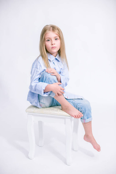 Beautiful fashionable little girl with blond hair in jeans clothes on a white background in studio - Foto, Imagen
