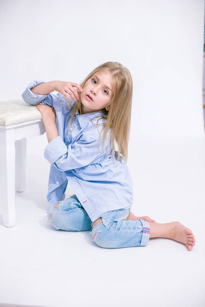 Beautiful fashionable little girl with blond hair in jeans clothes on a white background in studio - Zdjęcie, obraz