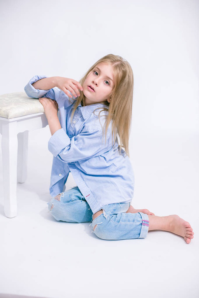Beautiful fashionable little girl with blond hair in jeans clothes on a white background in studio - Fotografie, Obrázek