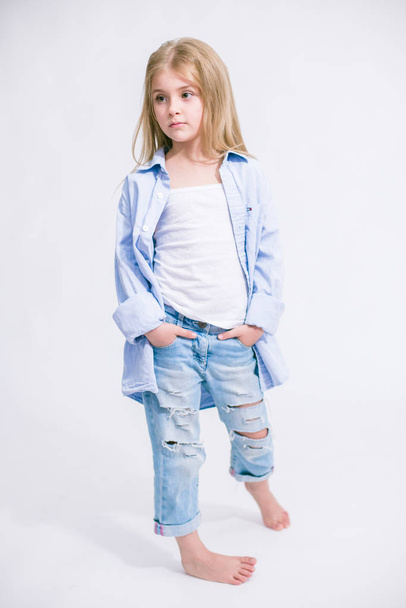 Beautiful fashionable little girl with blond hair in jeans clothes on a white background in studio - Fotó, kép