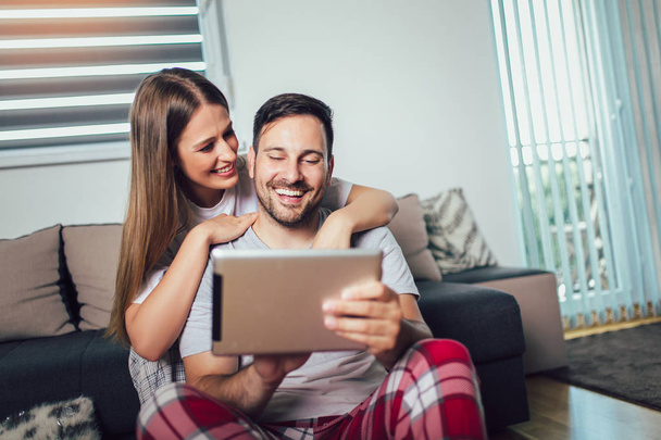 Couple joyeux en utilisant une tablette en ligne assis dans le salon
 - Photo, image