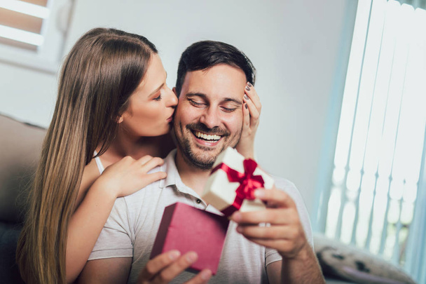 Vrouw verrassen zijn vriendje met een geschenk op de Bank thuis  - Foto, afbeelding