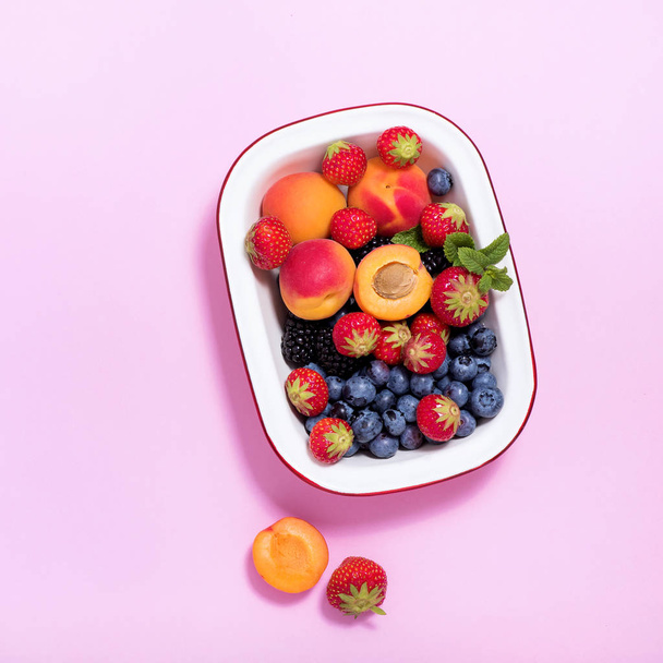 Ripe apricots and summer berries in a bowl on pink paper backgro - Photo, Image