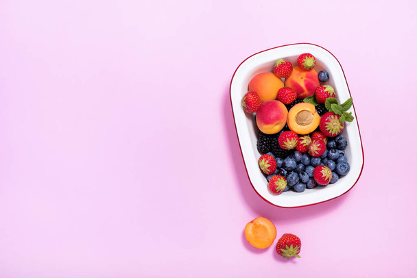 Ripe apricots and summer berries in a bowl on pink paper backgro - Foto, Bild