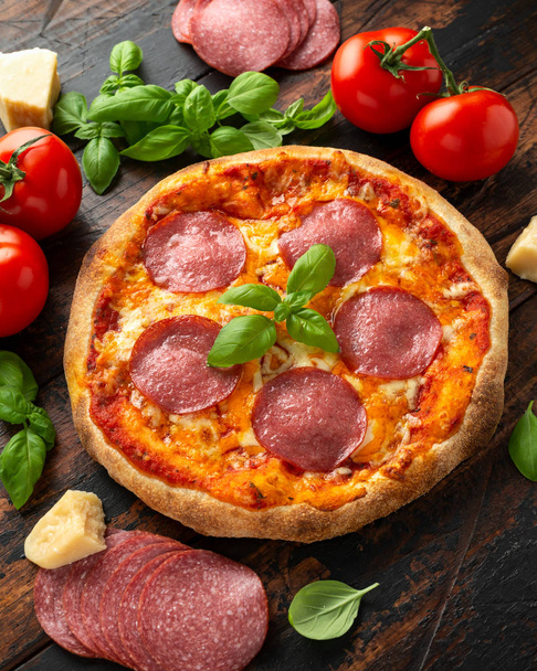 Zelfgemaakte pepperoni, salami pizza met basilicum, tomaten, kaas op houten tafel. klaar om te eten - Foto, afbeelding