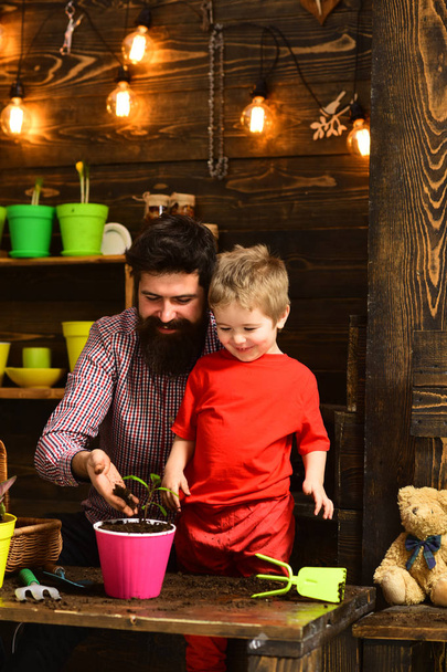 happy gardeners with spring flowers. bearded man and little boy child love nature. Flower care watering. Soil fertilizers. Family day. Greenhouse. Father and son. Fathers day. Revel in beauty - Valokuva, kuva