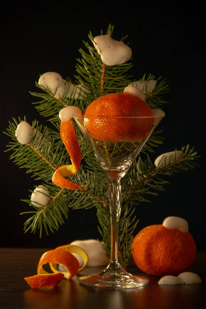 Dojrzały mandaryński ze skórką w kształcie spirali w szklance Martini, białym śniegu, pomarańczowym pomarańczy, gałęzi choinki, skórki w postaci spirali na czarnym tle. - Zdjęcie, obraz