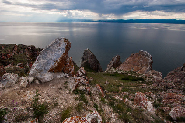 Скелі трьох братів на острові Ольхон на Байкському озері. Небо з хмарами. На каменях є червоний мох і зелена трава навколо. Йде дощ на відстані, гори видно. - Фото, зображення