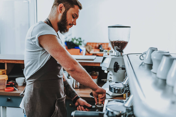 Concentrated barista using tamper and looking serious - Фото, зображення
