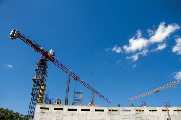 Red-blue crane near the wall of a multistory building under construction against the blue sky - Photo, Image